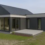 Nowoczesny dom z płyty warstwowej o ciemnoszarej elewacji, z dużymi przeszkleniami i betonowym tarasem.