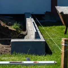 Budowa fundamentu pod ogrodzenie. Betonowe bloczki tworzą solidną podstawę, a poziomica i sznurek pomagają w precyzyjnym ułożeniu.