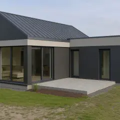 Nowoczesny dom z płyty warstwowej o ciemnoszarej elewacji, z dużymi przeszkleniami i betonowym tarasem.