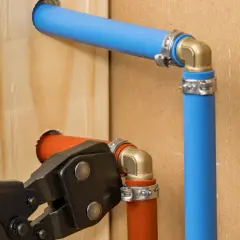Instalacja hydrauliczna z rurami pex. Narzędzie do zaciskania łączy pomarańczową rurę z mosiężnym kolankiem.