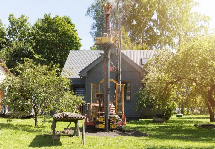 Wiertnica pracuje na działce, budując studnię. W tle widać dom i drzewa.