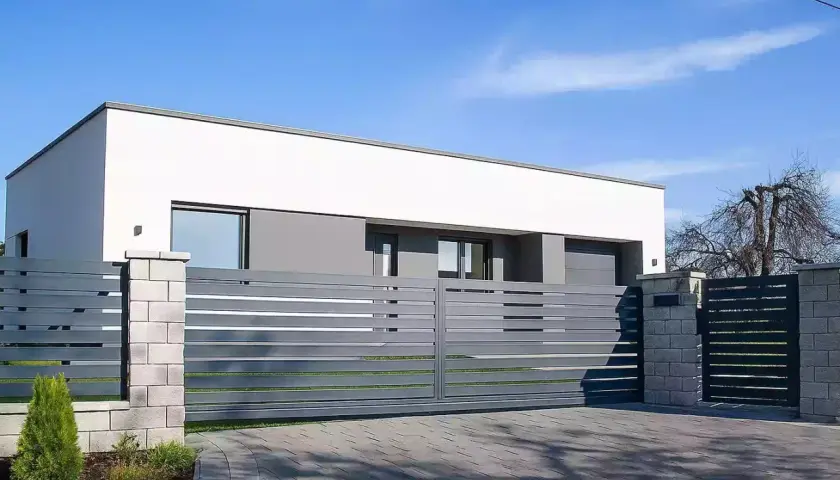 Nowoczesna, szara brama przesuwna z poziomymi listwami, prowadząca do minimalistycznego domu z białym tynkiem.