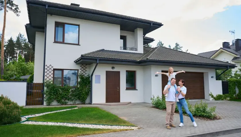 Szczęśliwa rodzina przed nowoczesnym domem. Czy to odzwierciedla realny koszt budowy domu?