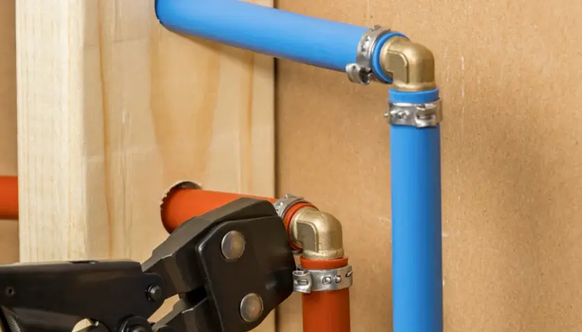 Instalacja hydrauliczna z rurami pex. Narzędzie do zaciskania łączy pomarańczową rurę z mosiężnym kolankiem.