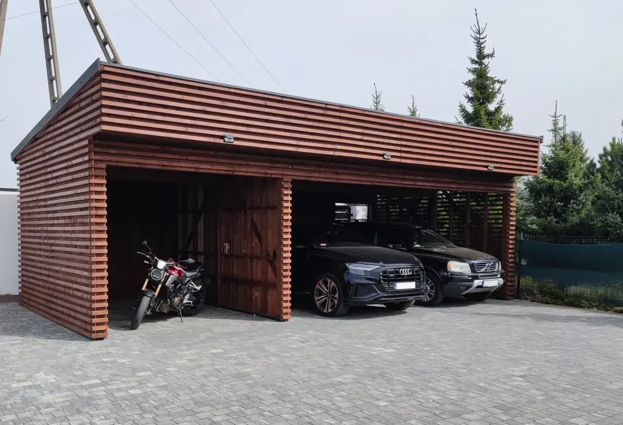 Drewniana wiata bez pozwolenia, z motocyklem i dwoma czarnymi samochodami.