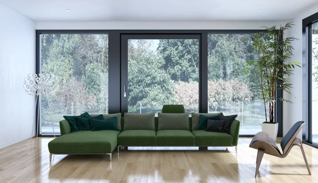 Nowoczesny salon z zieloną kanapą i designerskim fotelem, a wszystko to otoczone przez imponujące okna panoramiczne z widokiem na ogród.