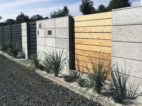 Nowoczesne ogrodzenie z bloczków betonowych i drewna, z elementami metalowymi i zielenią.